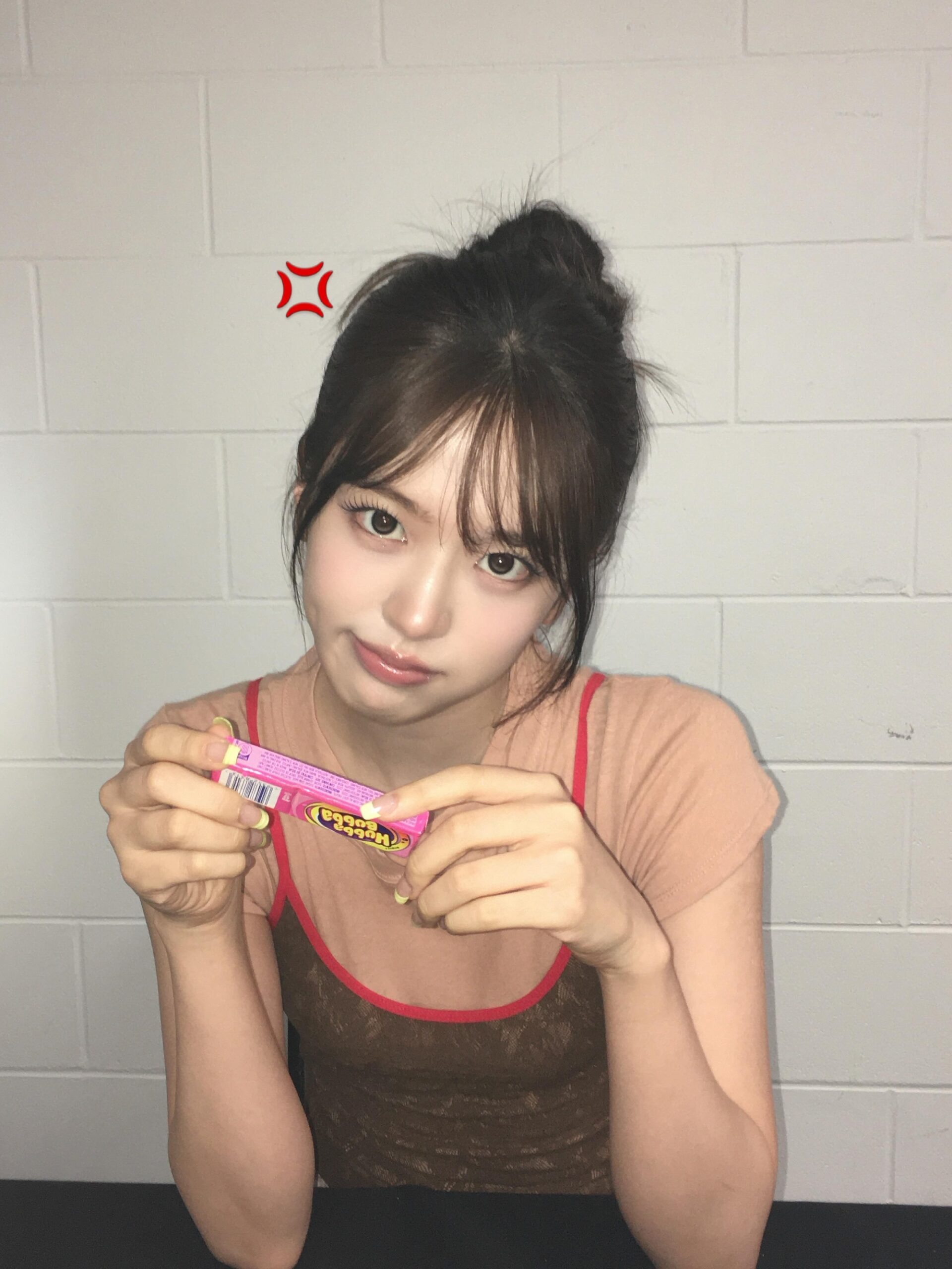 An Yujin seen with arms crossed, holding bubblegum and posing in a cute strappy camisole