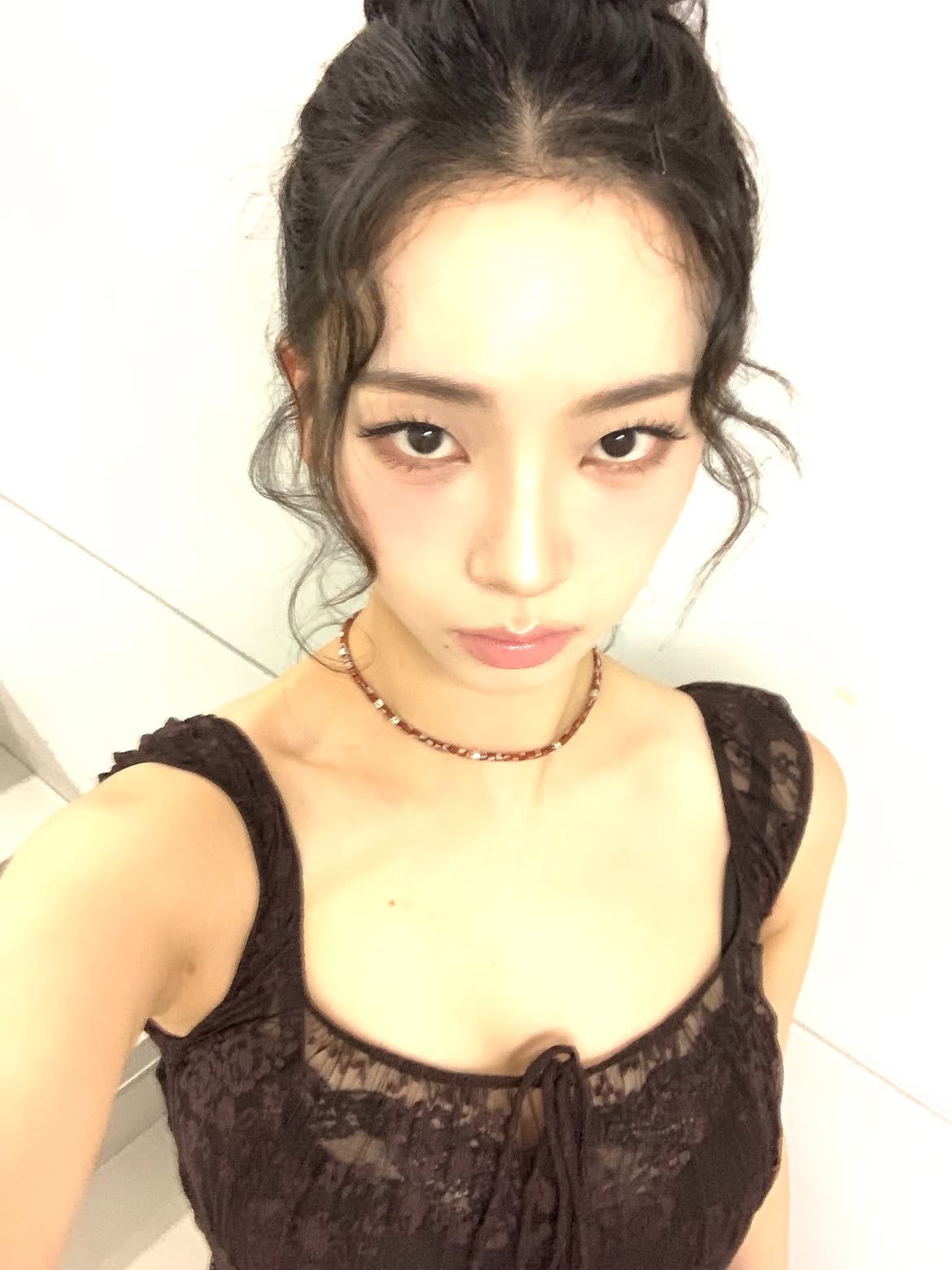 Karina in a black sheer dress crouching down, chest area - Instagram