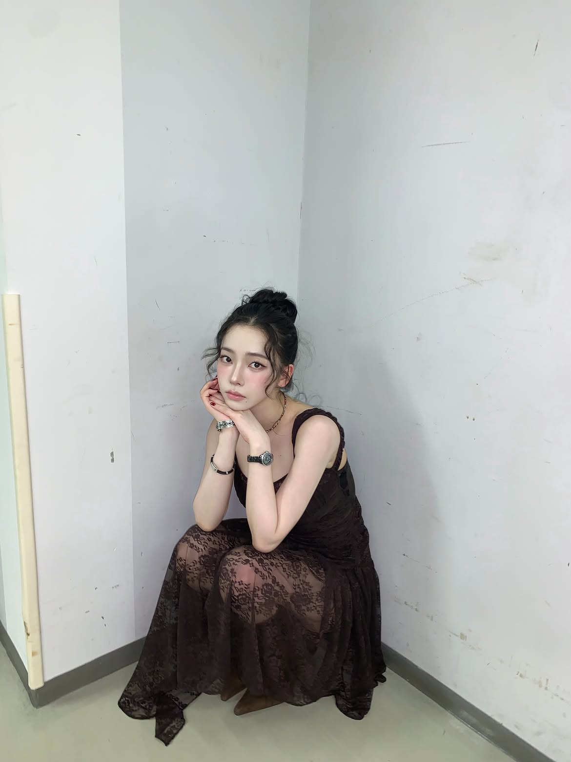 Karina in a black sheer dress crouching down, chest area - Instagram