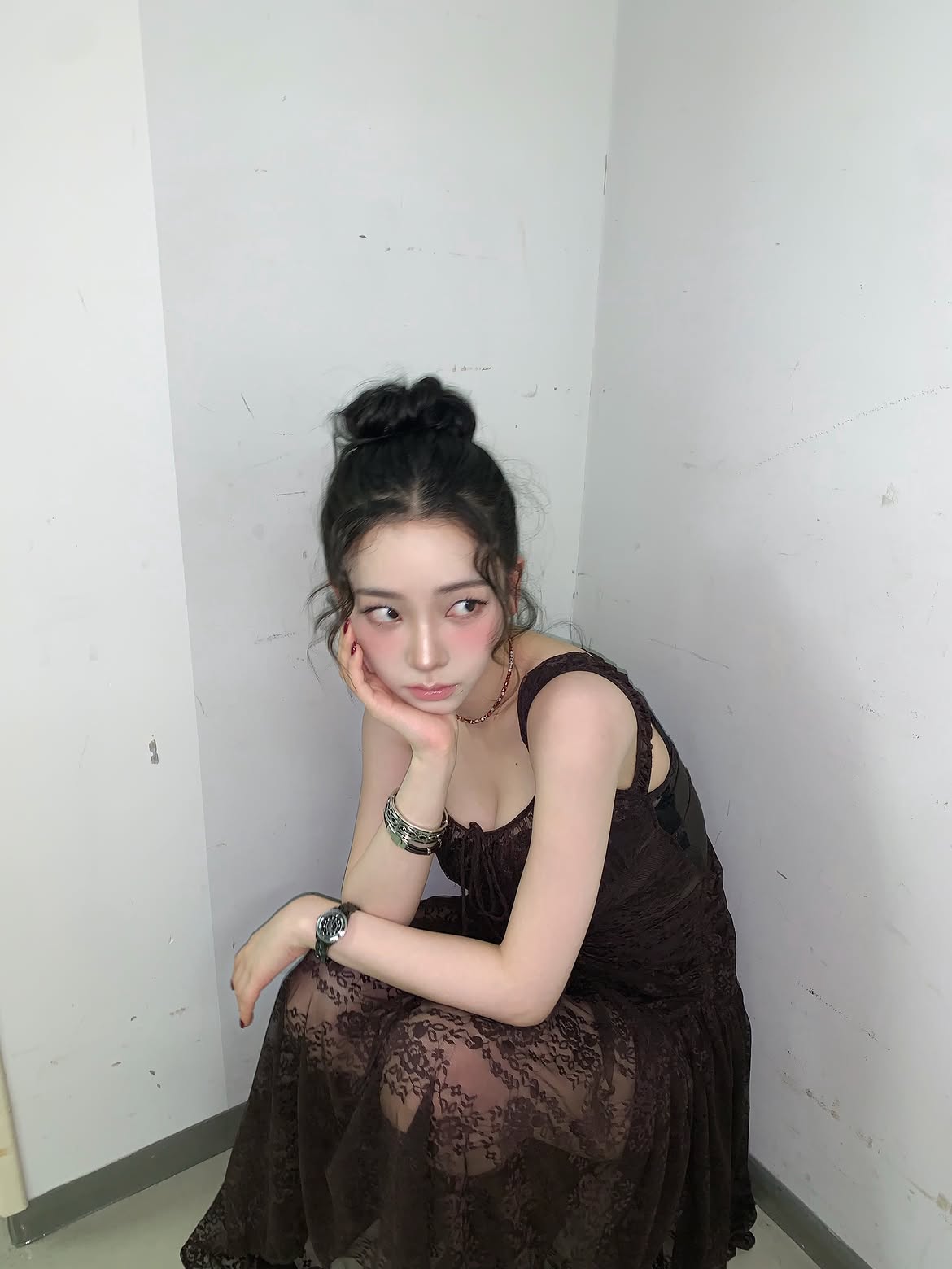 Karina in a black sheer dress crouching down, chest area - Instagram
