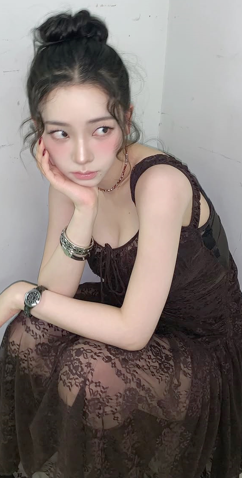 Karina in a black sheer dress crouching down, chest area - Instagram